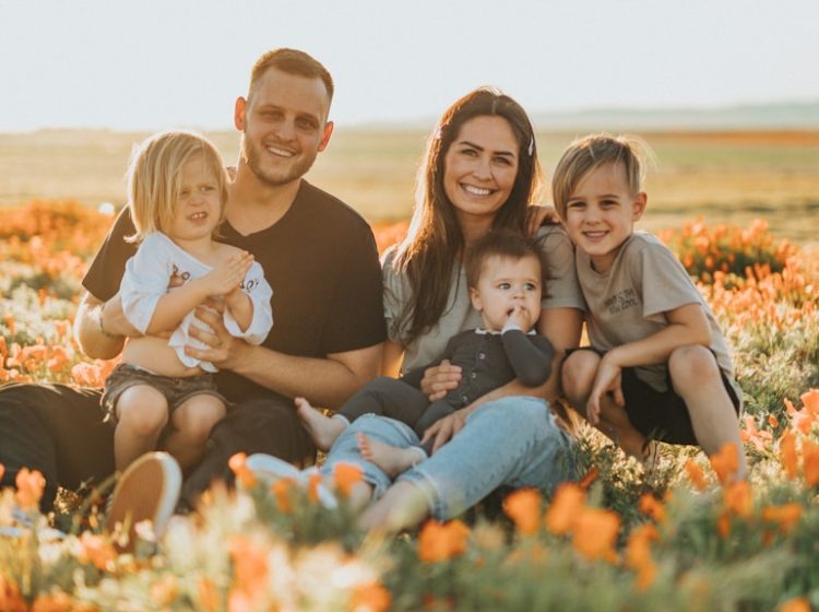 3 women and 2 men sitting on green grass field during daytime